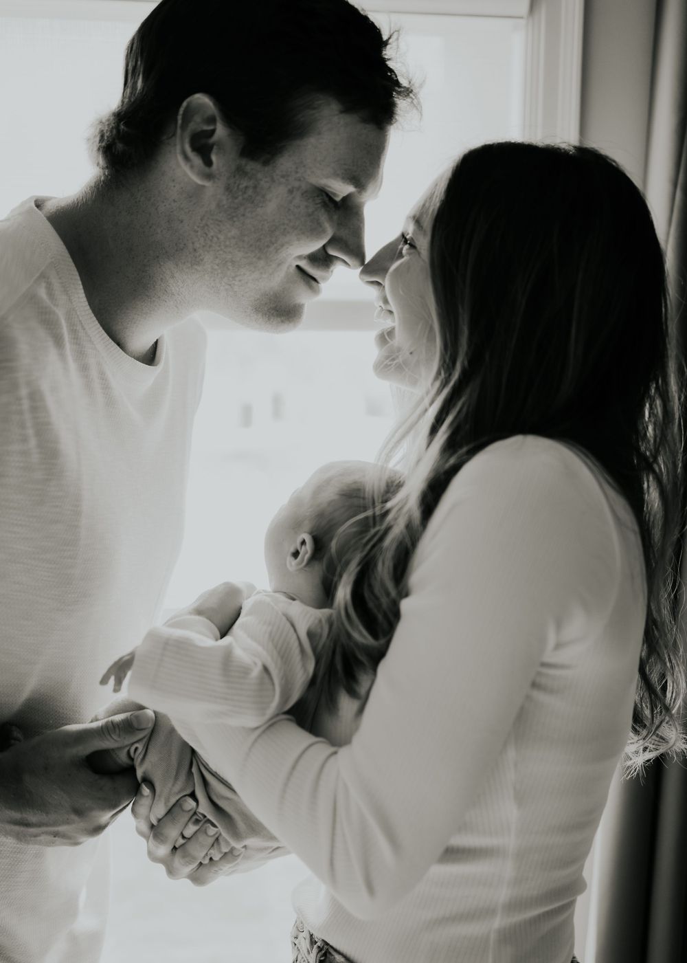 Black and white intimate portrait of a couple sharing a tender moment while holding their baby.