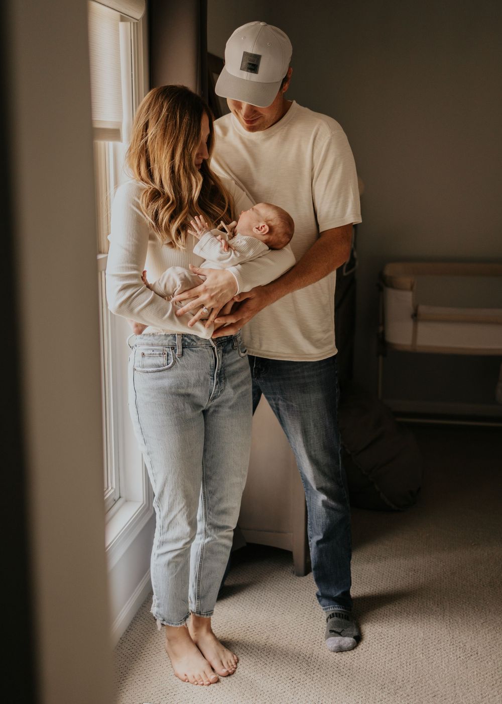 A tender family moment by a window as parents cradle their newborn baby in a naturally lit room.