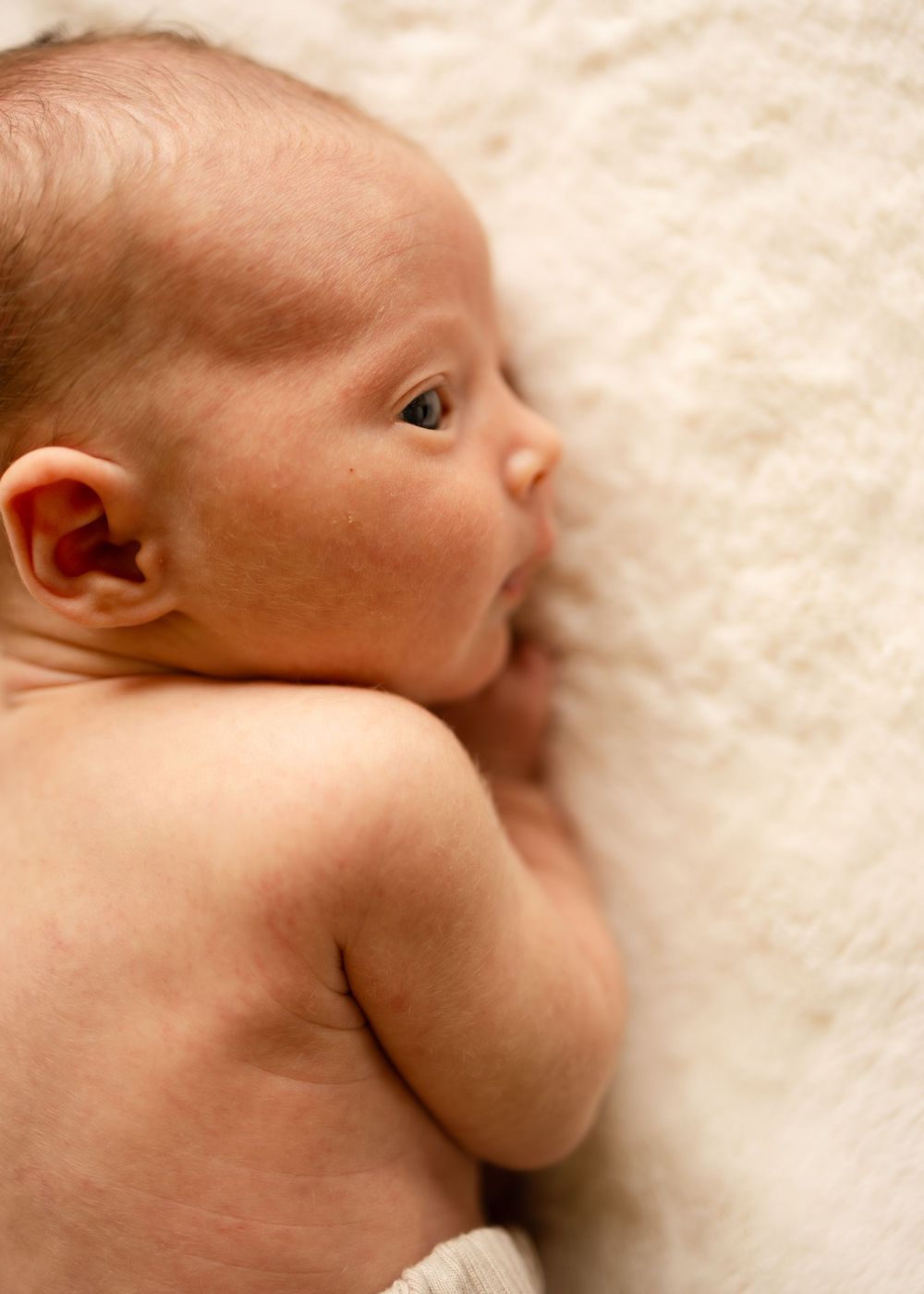 Close-up profile of a newborn baby lying on white bedding.