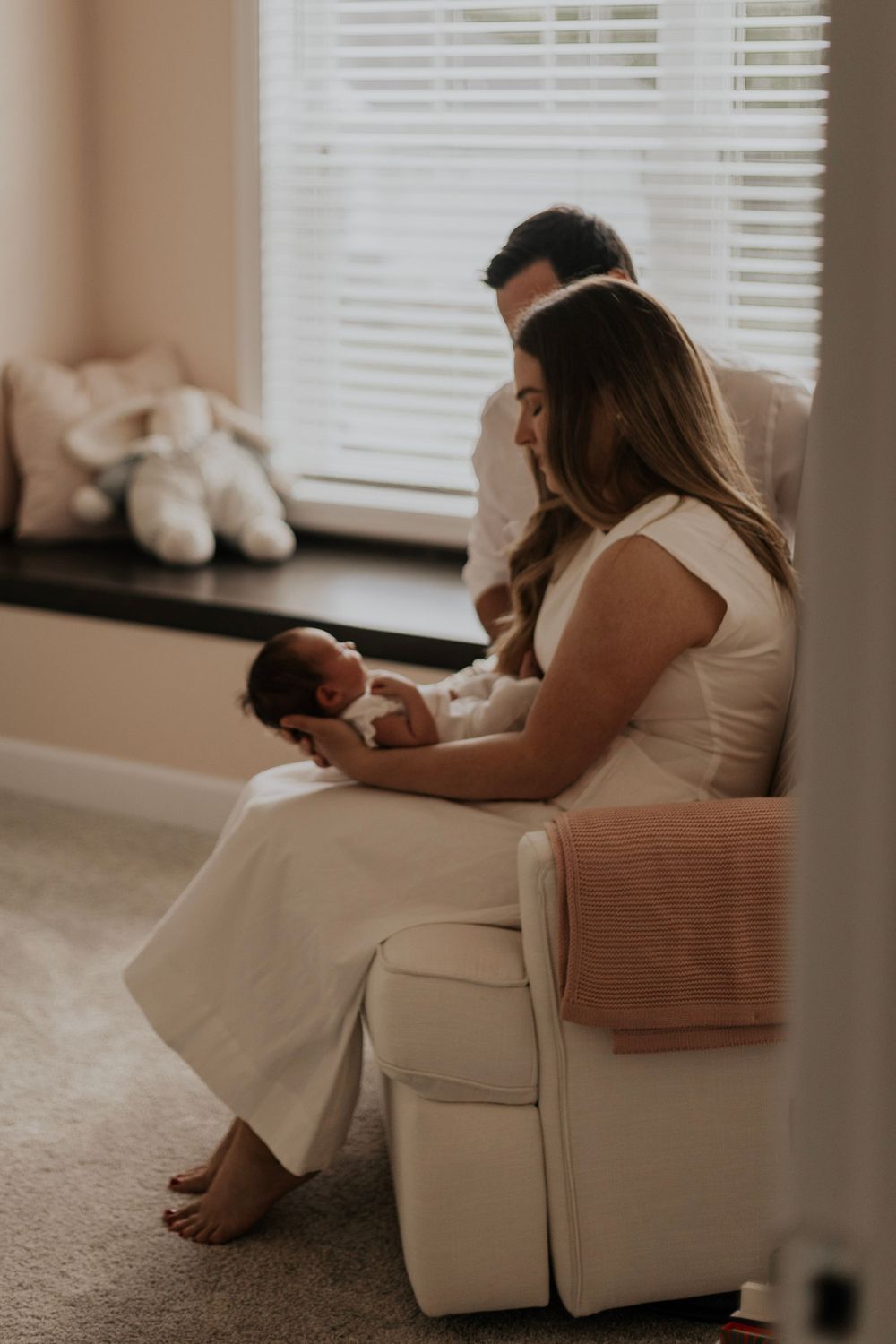 Intimate family moment with newborn baby in a nursery by window with soft natural light.