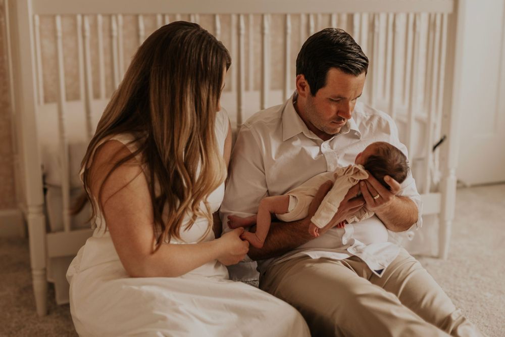 Parents sharing tender moment with newborn baby in nursery setting.
