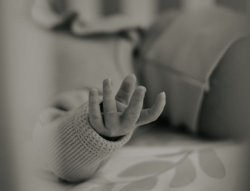 Black and white macro shot of baby's tiny hand reaching upward.