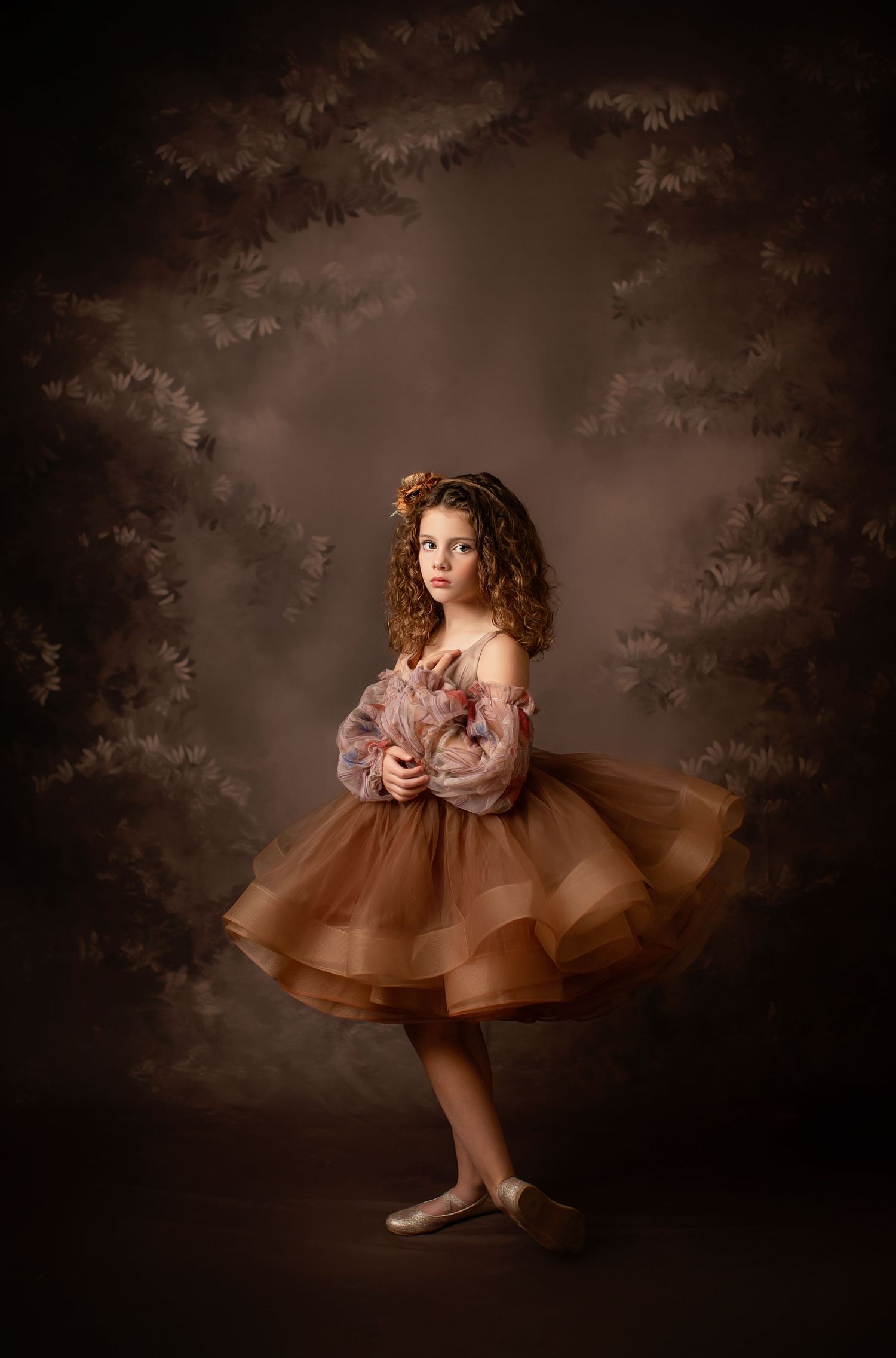 Flowing copper-colored ballgown with tulle layers photographed against dramatic studio backdrop.