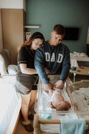 Hospital room scene showing parents caring for newborn baby in medical setting.