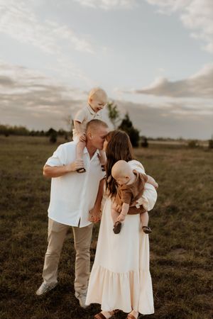 Family shares tender moments together in a golden field at sunset.