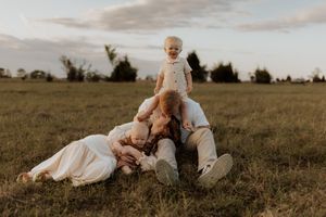 Family plays and relaxes together on grassy field during sunset photoshoot.
