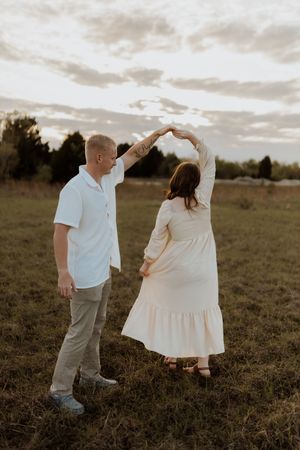 Couple dances together in casual attire against sunset sky in open field.