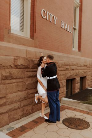 Romantic couple embracing outside brick City Hall building.