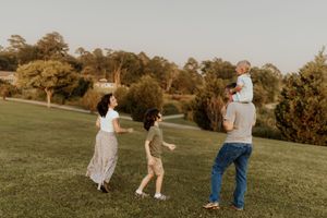 Joyful family moment playing together on a grassy hillside at sunset.