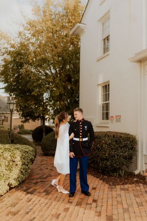 Marine in dress blues and bride in white dress pose together on brick pathway.