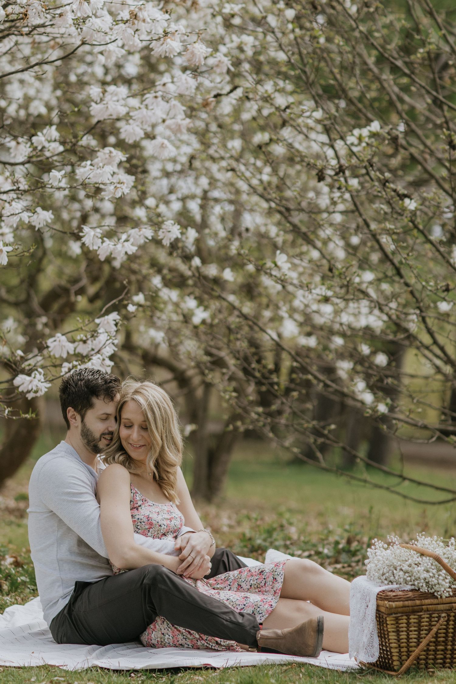 Couple sharing intimate moments while relaxing on a picnic blanket under flowering cherry trees.