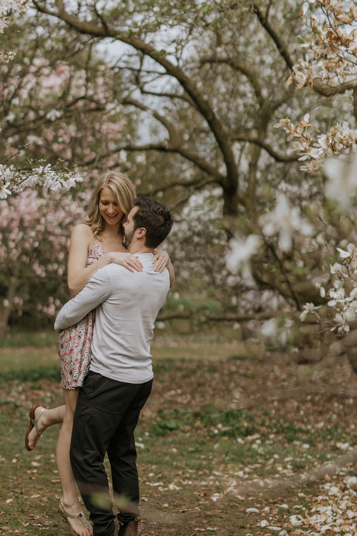 Playful couple embracing and dancing under blooming cherry trees in spring.