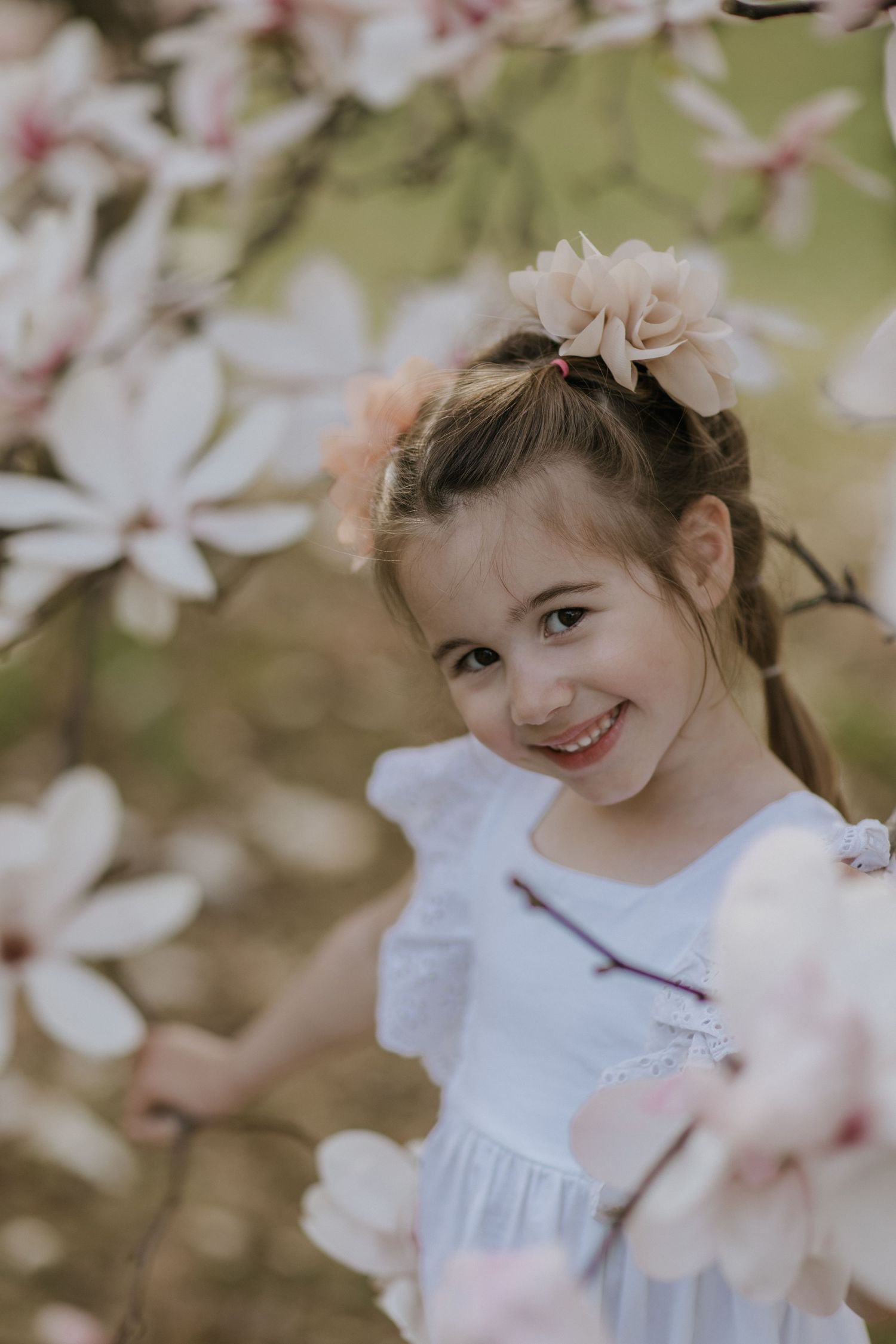 Young girl smiling sweetly among delicate spring cherry blossoms.
