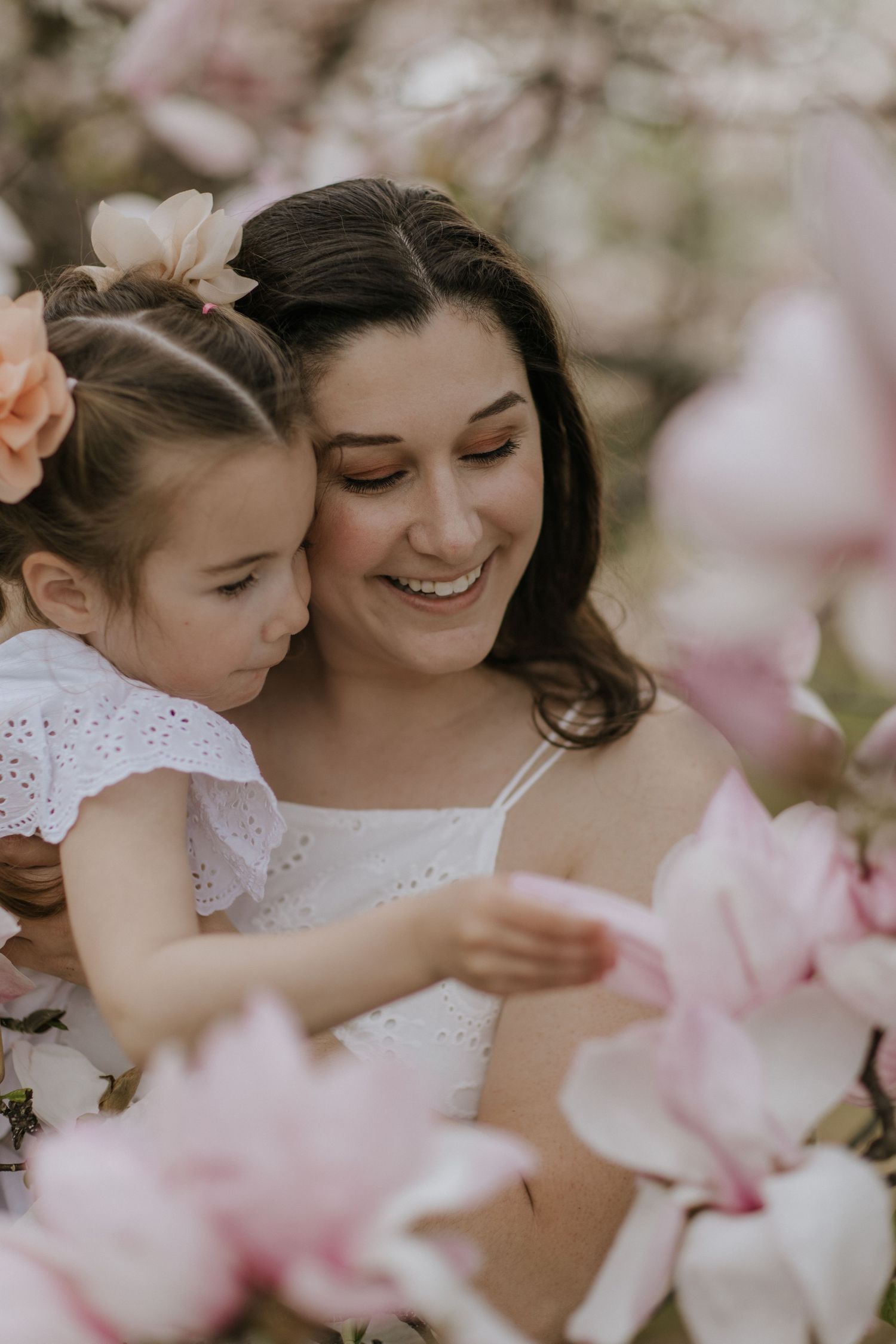 Joyful mother-daughter moment captured among pink spring blossoms.