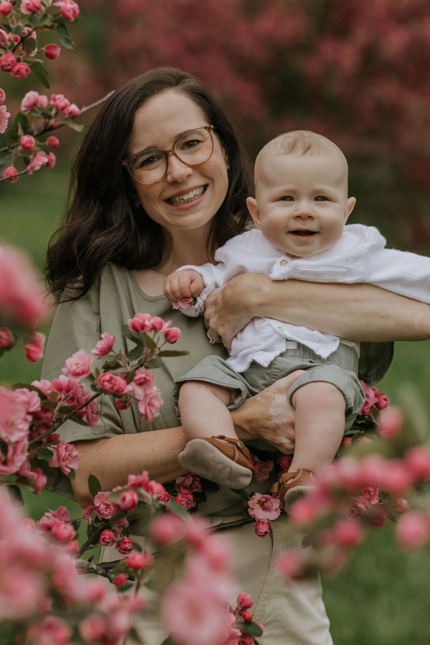 Mother and baby portrait among pink cherry blossoms during spring photo session.