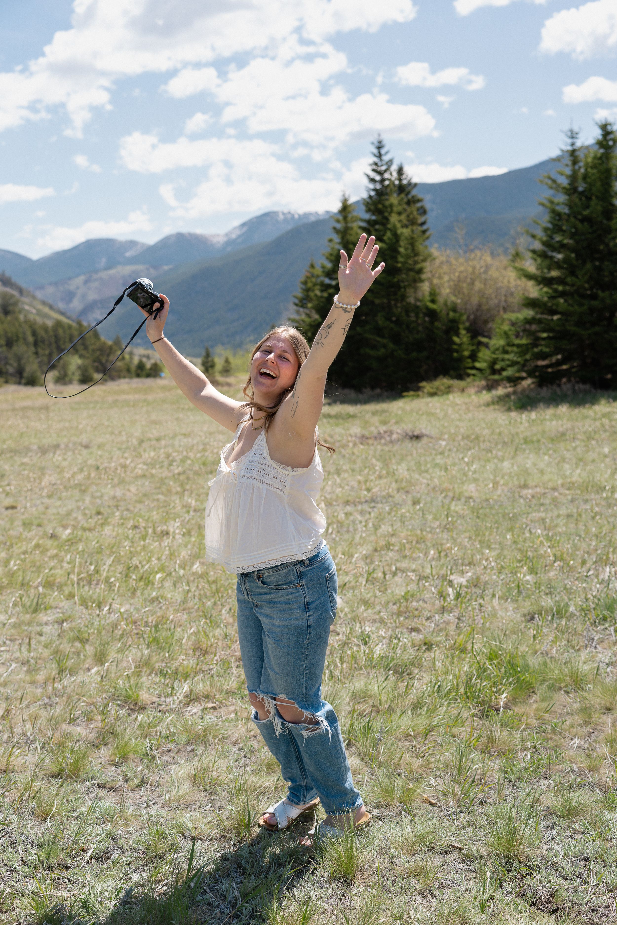 Iowa Midwest wedding and senior photographer with camera in right hand - hands in the air, fun and with mountains behind.