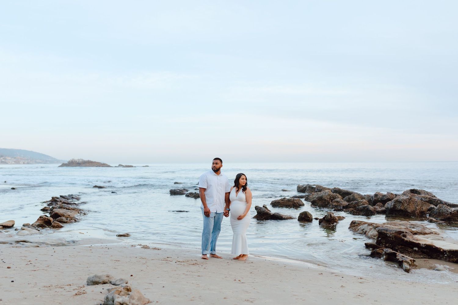 A couple walks along rocky beach shoreline at sunset.