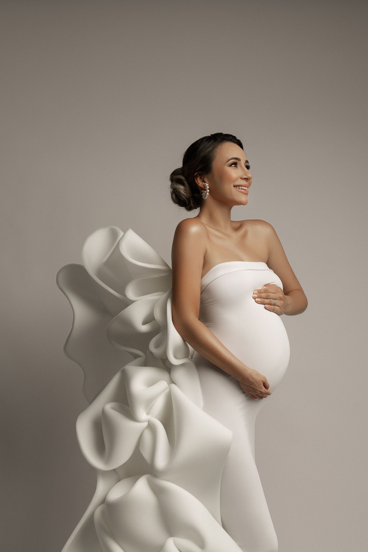 Elegant maternity portrait featuring sculptural white dress with dramatic ruffled details.