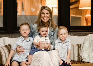 A family group wearing matching gray outfits sits together on a couch in a warmly lit room.