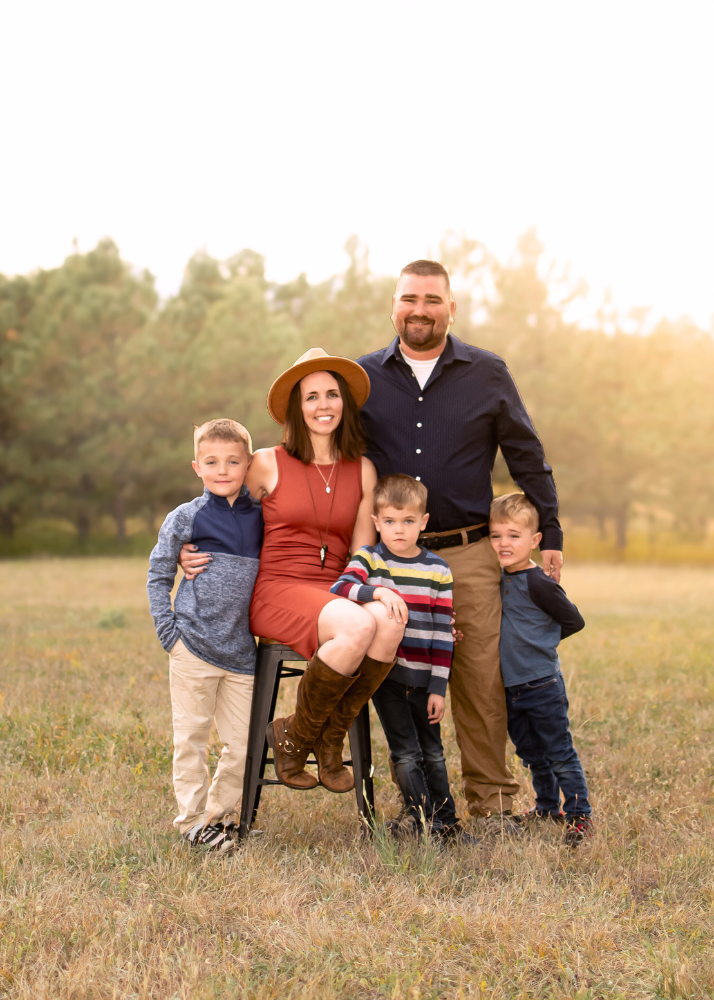 A family of five poses together in a grassy field during golden hour sunset.