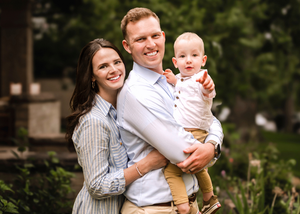 A trio poses outdoors together near greenery and stone steps in casual attire.