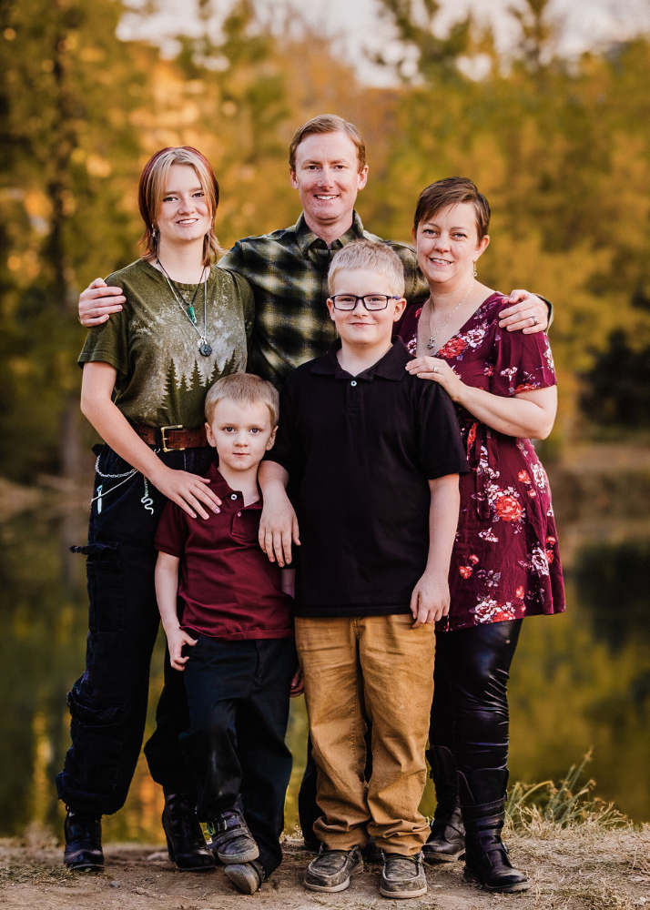 A family of five poses together outdoors during autumn with a warm sunset glow and trees in the background.
