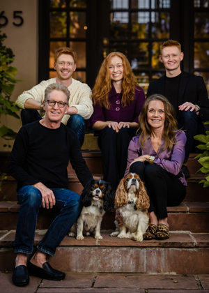 A family portrait on outdoor steps with two small dogs including a Cavalier King Charles Spaniel in the center.
