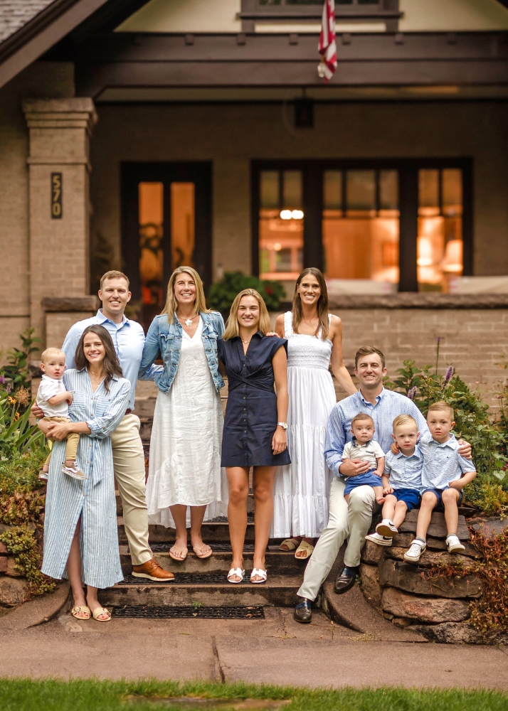 A group stands together on stone steps of a craftsman style home during a warm evening photoshoot.