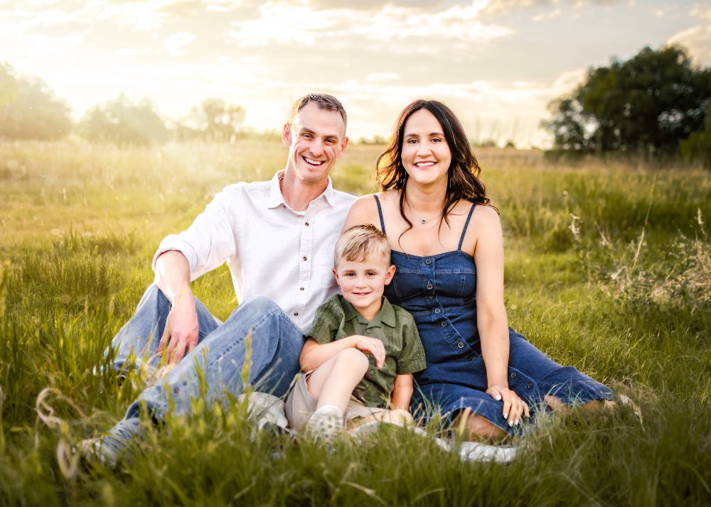 Family sitting together on a blanket in a sunlit meadow during golden hour.