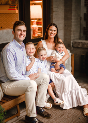 A beautifully dressed family of five sits together on a wooden porch bench during a portrait session.