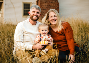 A family sits together in a rustic outdoor setting with tall grass during golden hour.