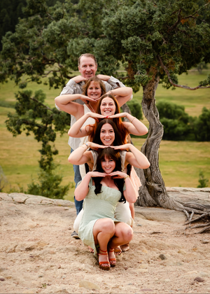 A group poses creatively on a hill making framing gestures with their hands against a scenic natural backdrop.