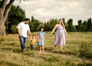 Joyful family walking together in rural meadow on sunny summer day during outdoor photo session.