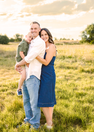 Family portrait taken in a golden sunlit field at sunset with tall grass and warm lighting.