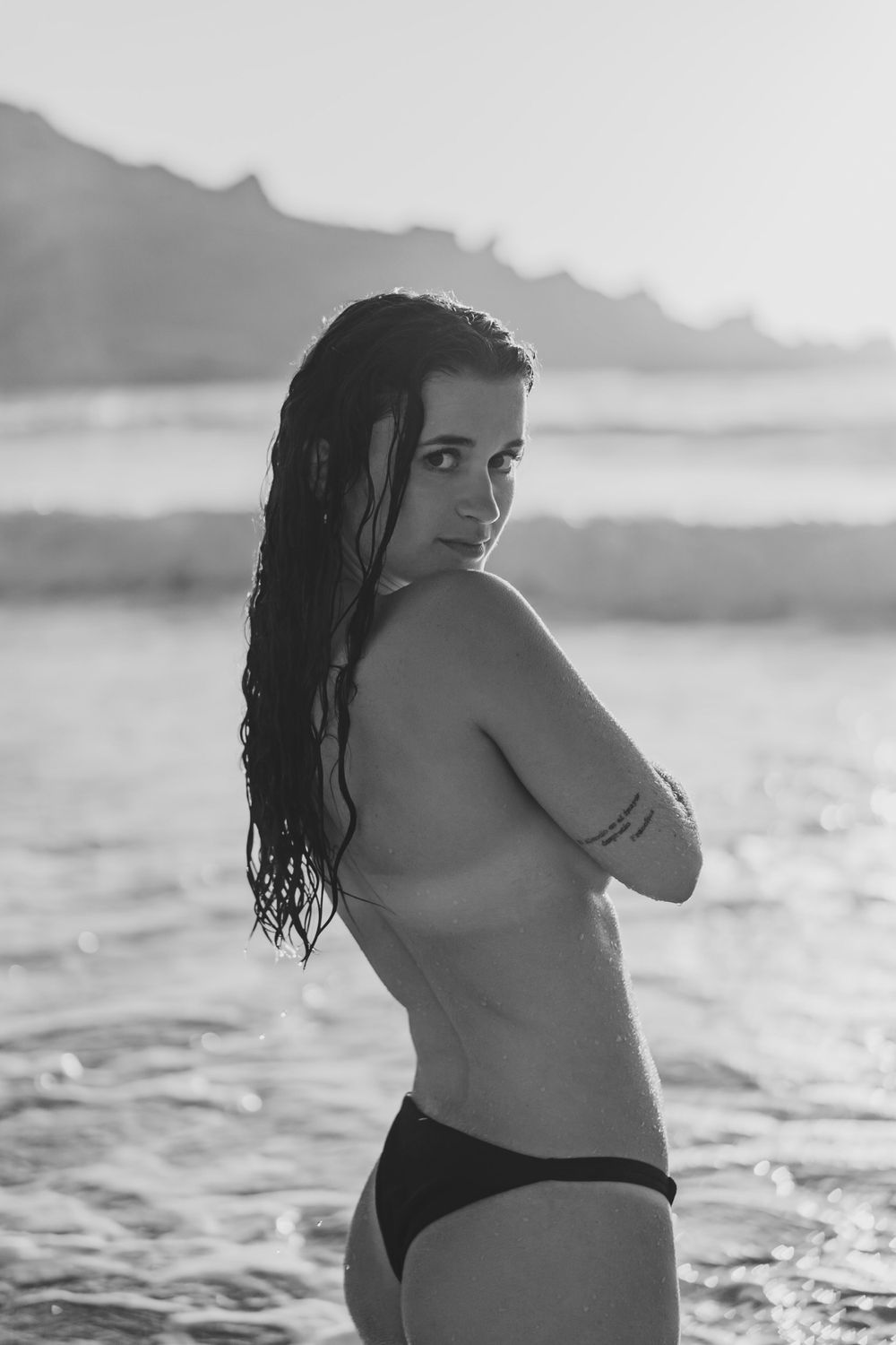 portrait lifestyle d'une jeune femme topless de dos en noir et blanc, à la plage en extérieur