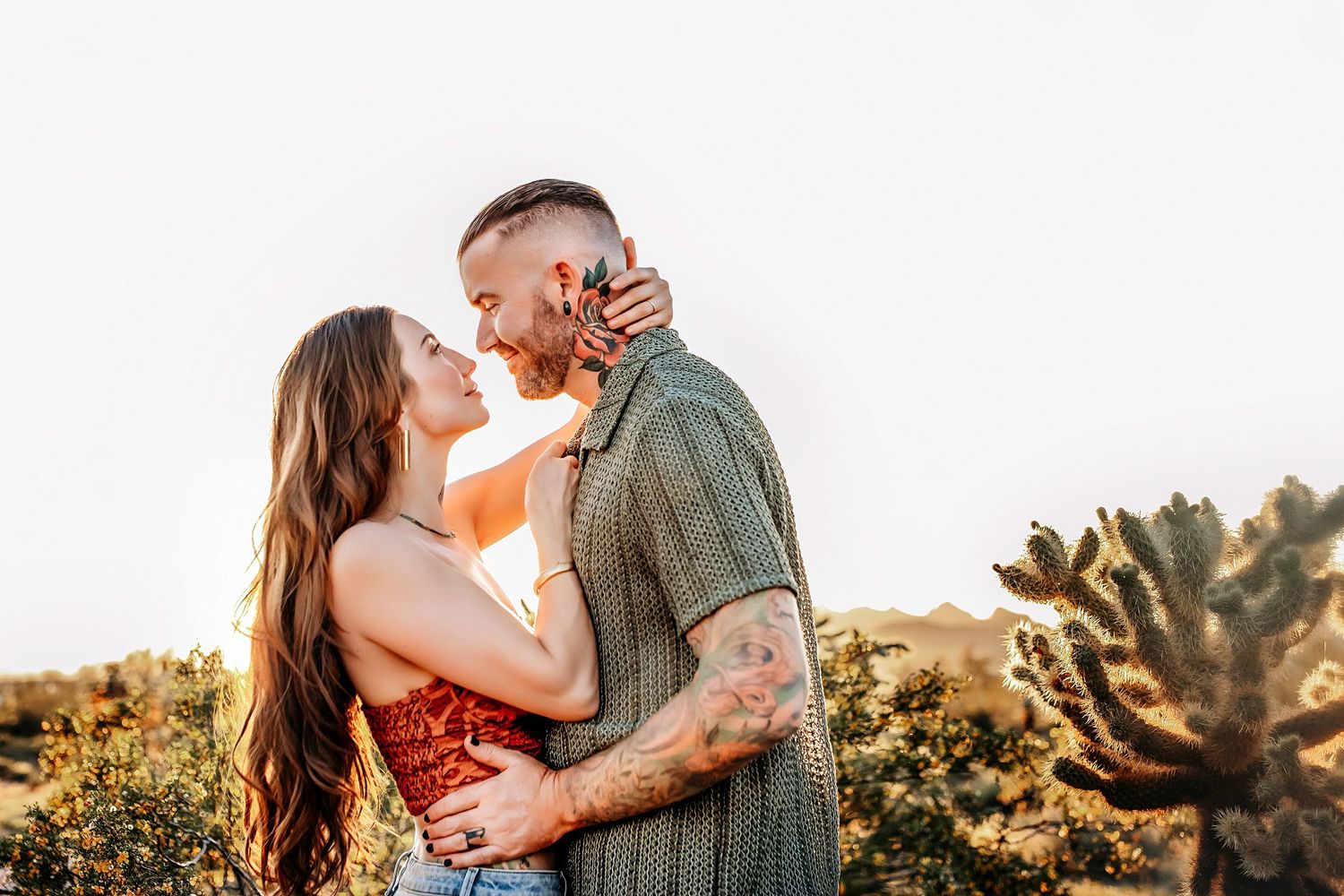Couple embracing in desert landscape during golden hour with cactus in background.