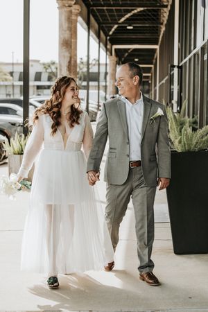 Newlywed couple walking together under covered walkway in formal attire.