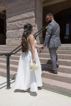 Wedding couple on stone steps with bride holding white bouquet in elegant attire.