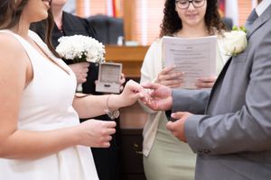 Wedding ceremony closeup of hands exchanging rings with white bouquet.