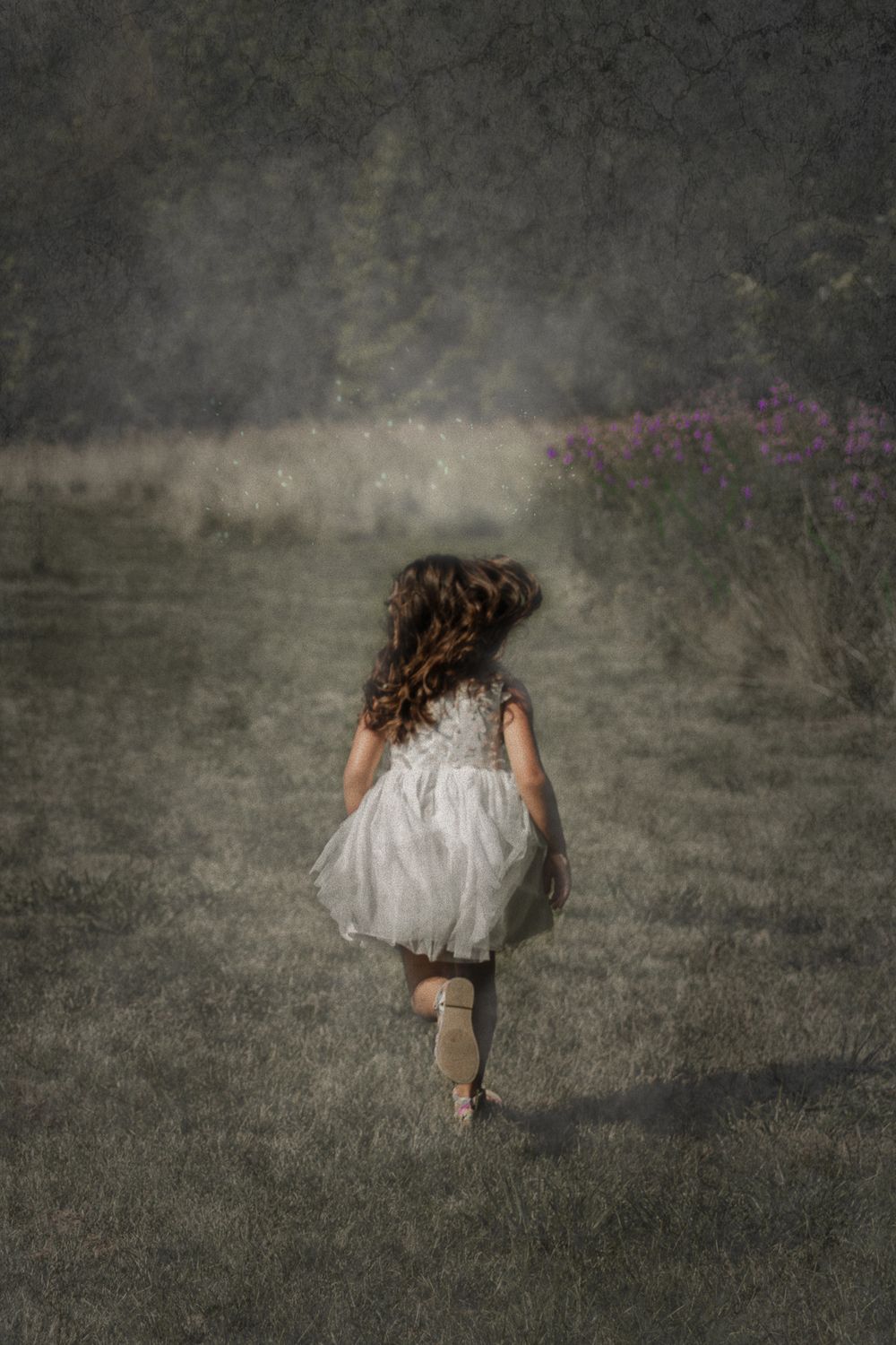 A dreamlike image of a child in a white dress running through a misty field with curly hair flowing.