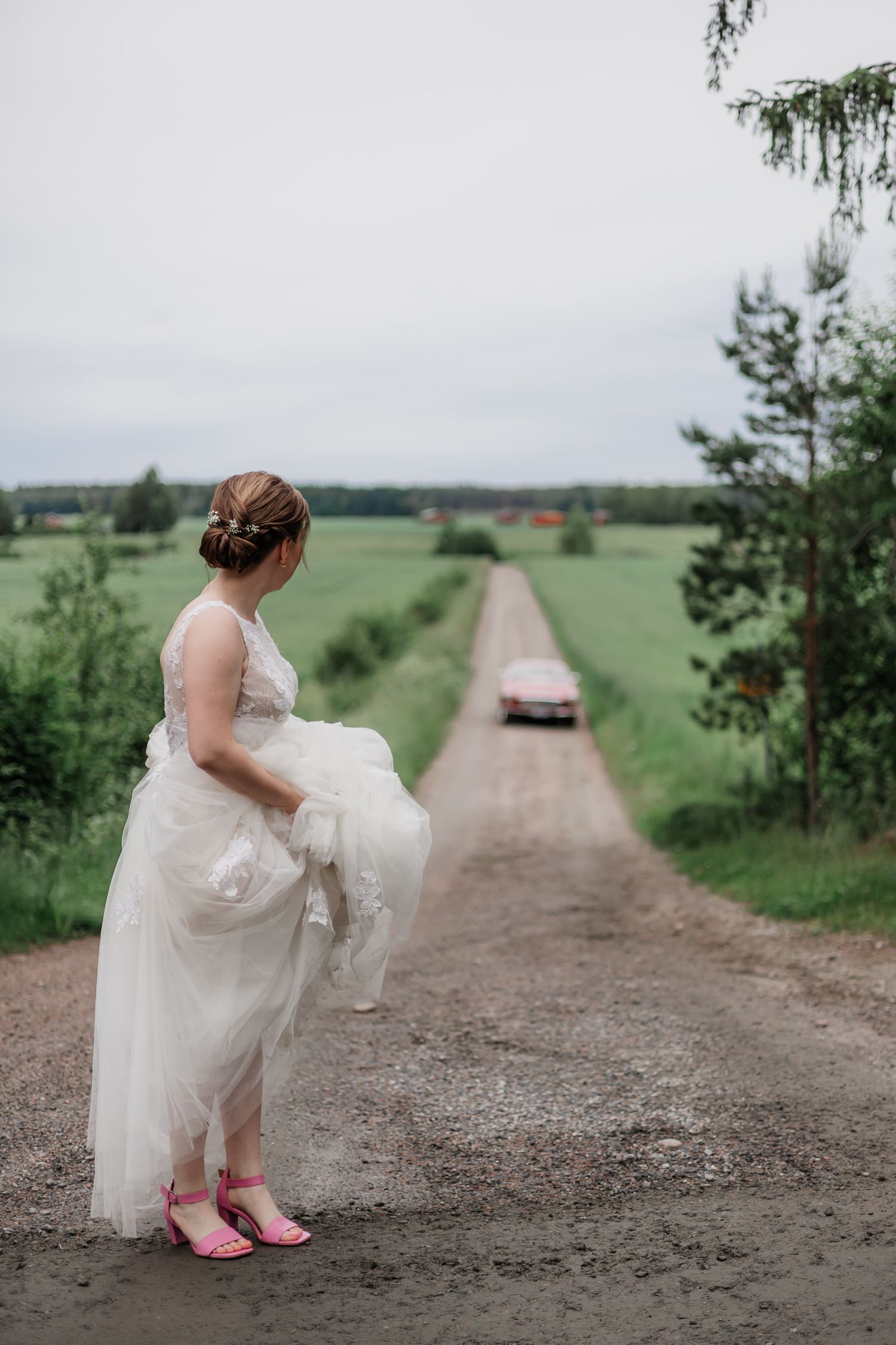 A person in a wedding dress and pink shoes walking down a rural dirt road.