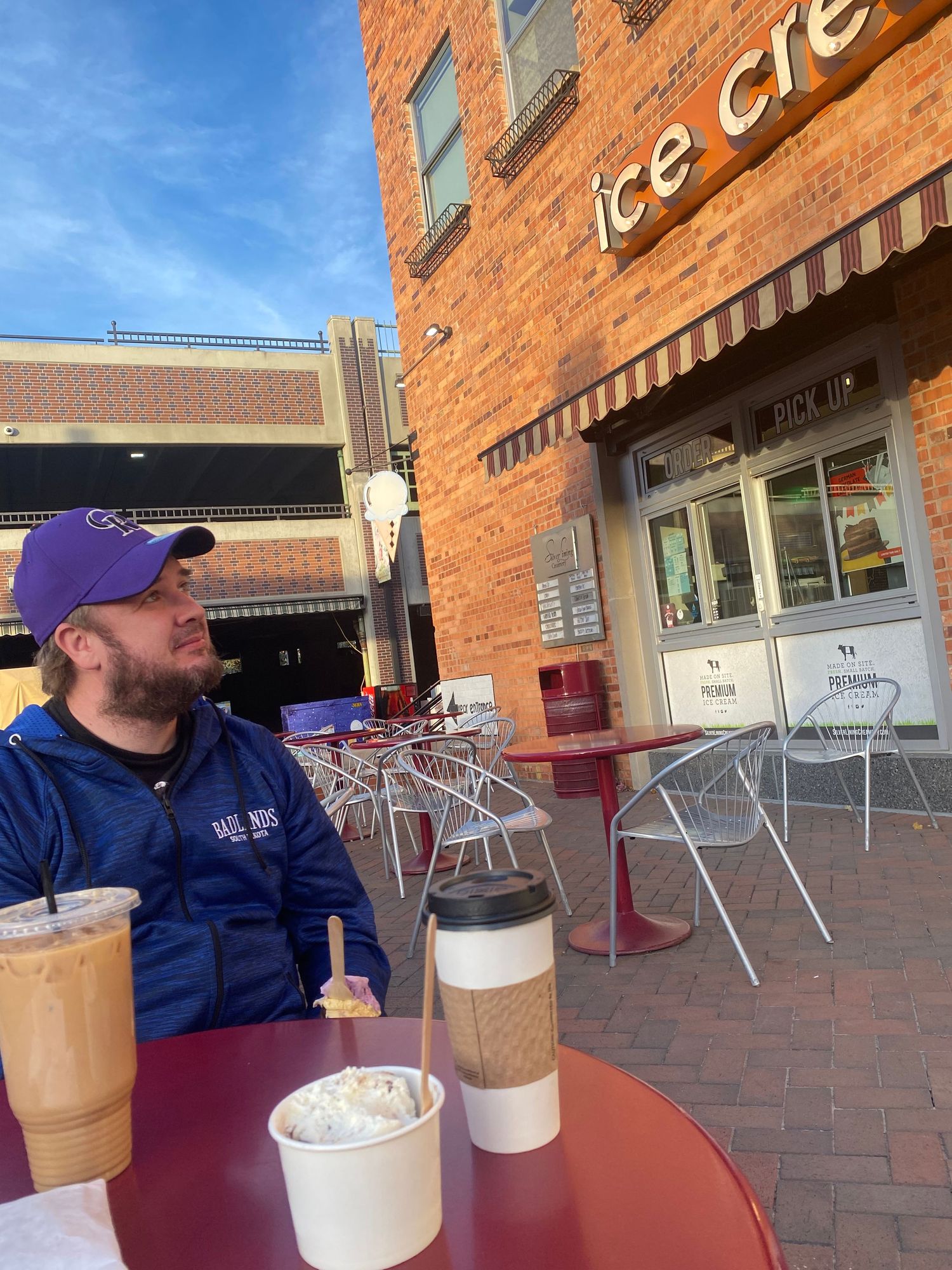 Coffee drinks on an outdoor cafe table with rustic brick wall and metal chairs in the background.