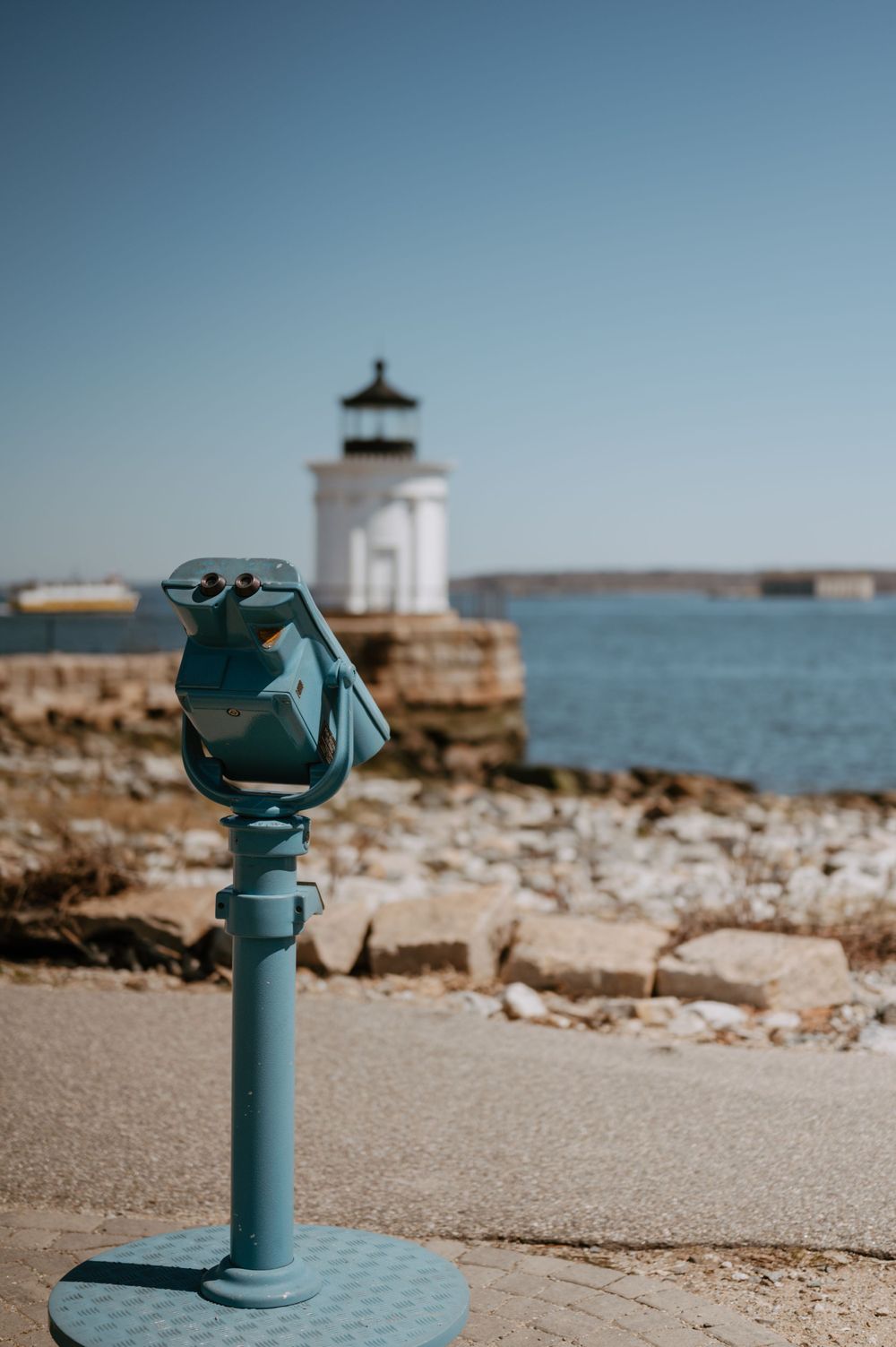 Blue viewfinder station with lighthouse in background at coastal viewpoint.