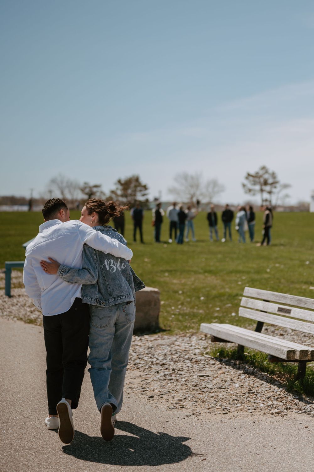 Couple walking arm in arm on path with group visible in background.