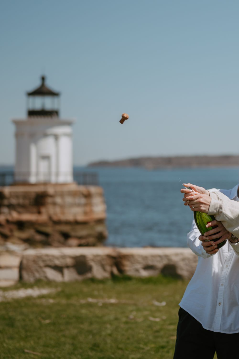 Champagne cork flying through air with lighthouse and ocean in background.