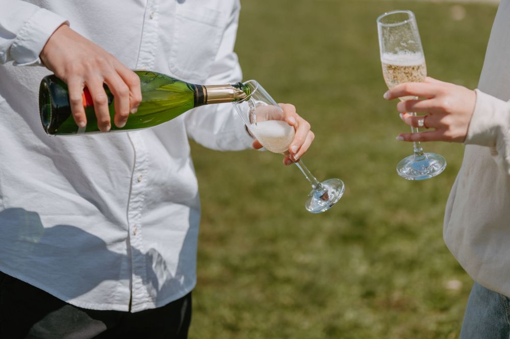 Champagne being poured between two glasses outdoors on a sunny day.
