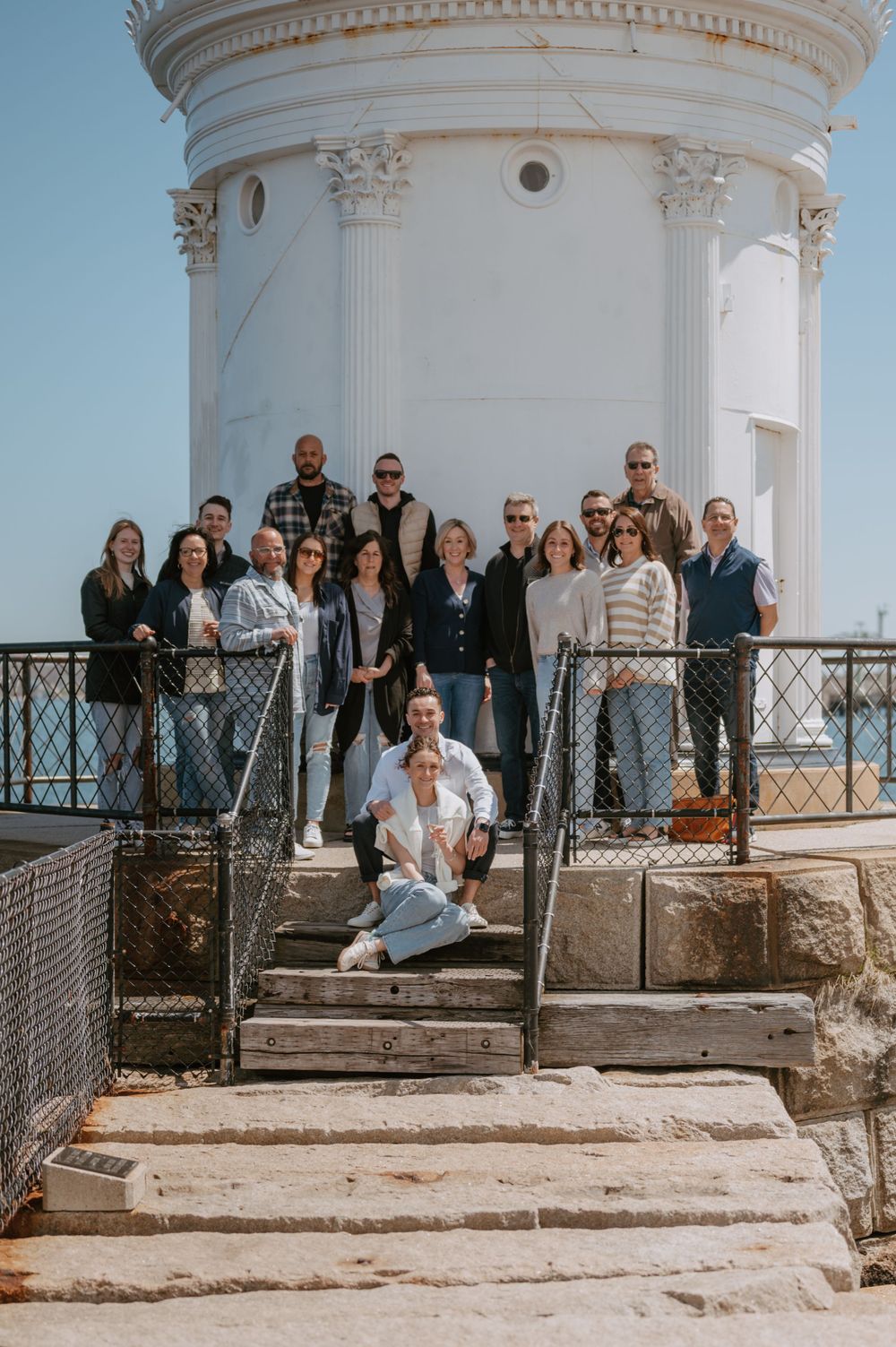 Group photo of people gathered on stone steps in front of white columned lighthouse structure.