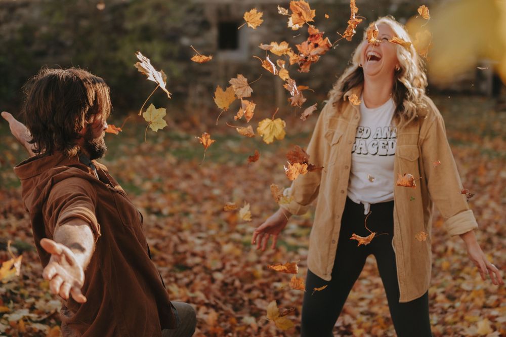 Two people playing with falling autumn leaves in a joyful outdoor scene.