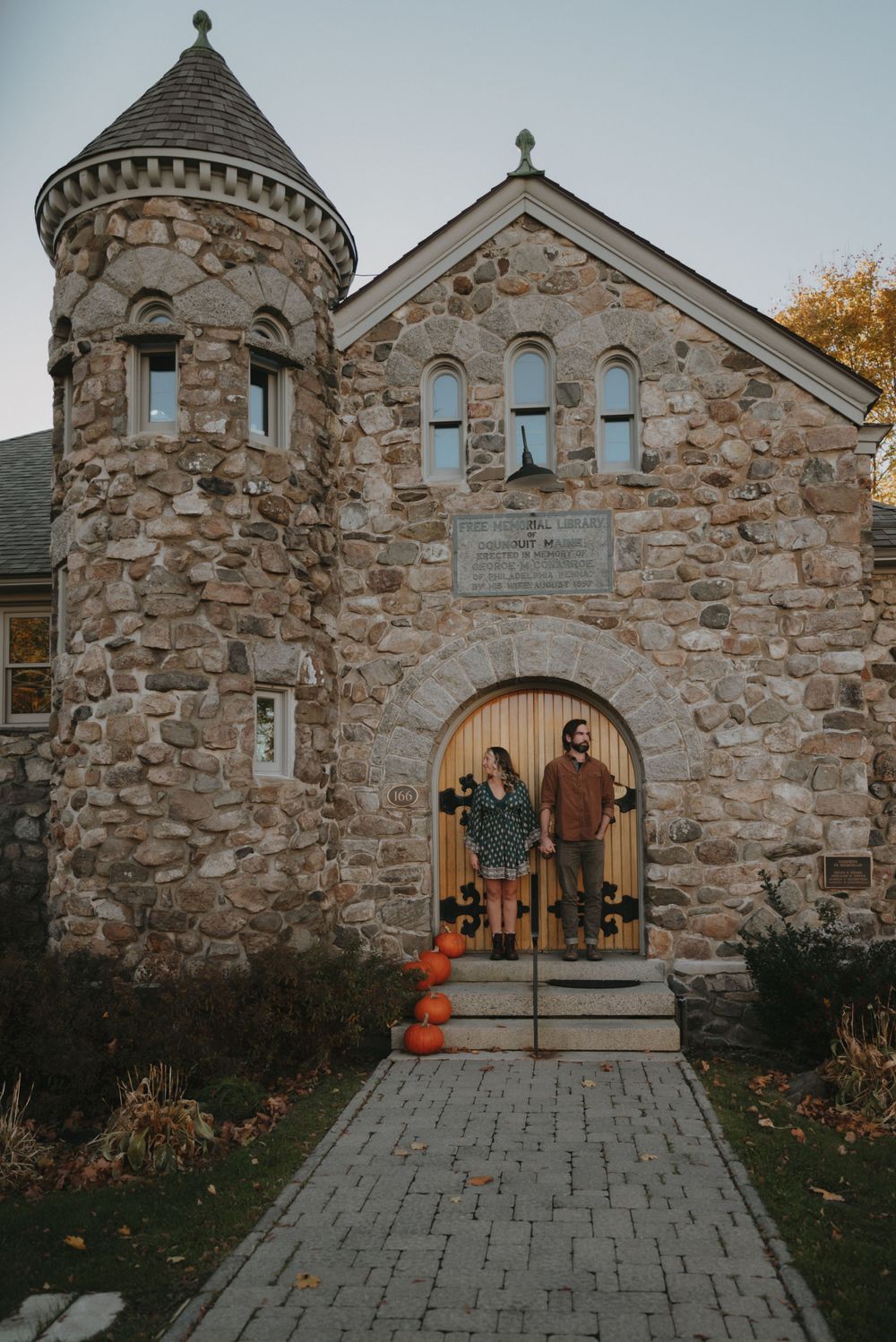 Stone church entrance decorated with pumpkins and fall decor along a brick path at sunset.