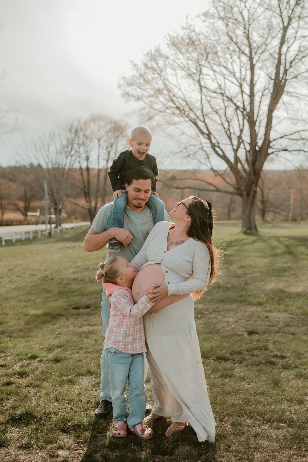 Pregnant woman and man with two young children enjoying a family moment outdoors on a sunny day in a green field.